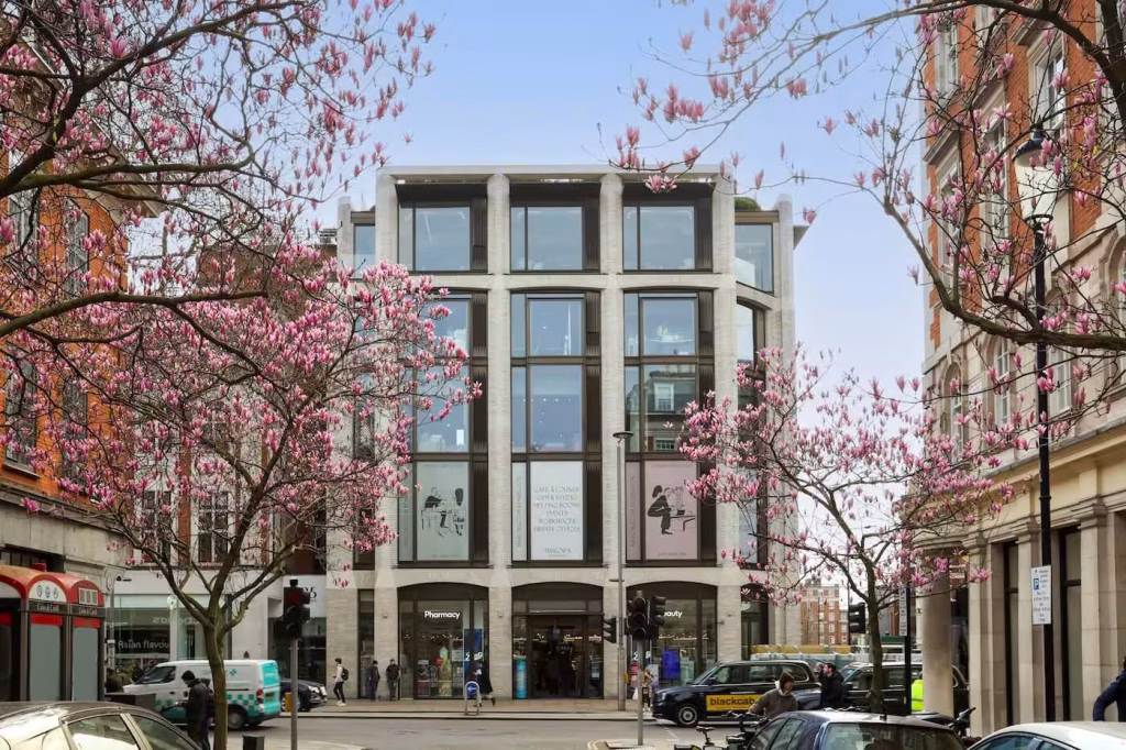 Maslows Kensington 6 Front view of Maslows Kensington framed by flowering trees, showing printed Contravision graphics across two floors.